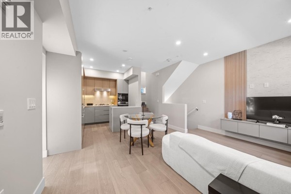 Living and dining area with a gray sofa, glass-top dining table, and a staircase. - 130 W Woodstock Avenue, Vancouver