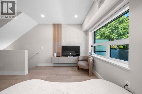 Living room with a television, armchair, and a large window with greenery outside. - 130 W Woodstock Avenue, Vancouver