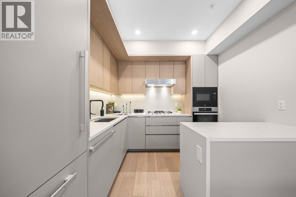 Modern kitchen with gray and wood cabinetry, white countertops, and stainless steel appliances. - 130 W Woodstock Avenue, Vancouver