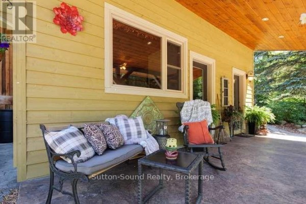 Covered front porch with cushioned seating, a rocking chair, and decorative pillows. - 130044 Sideroad 20 Side Road, Georgian Bluffs