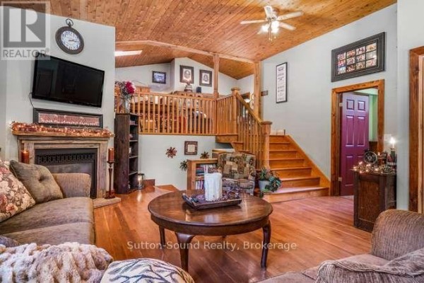 Living room with fireplace, sectional sofa, wood floors, and a wooden staircase. - 130044 Sideroad 20 Side Road, Georgian Bluffs