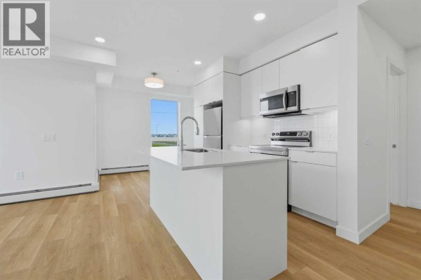 Bright kitchen with white cabinetry, stainless steel appliances, and quartz countertop with island. - 1301, 8500 19 Avenue, Calgary
