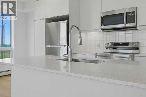 Close-up of kitchen island with quartz countertop, stainless steel faucet, and tile backsplash. - 1301, 8500 19 Avenue, Calgary