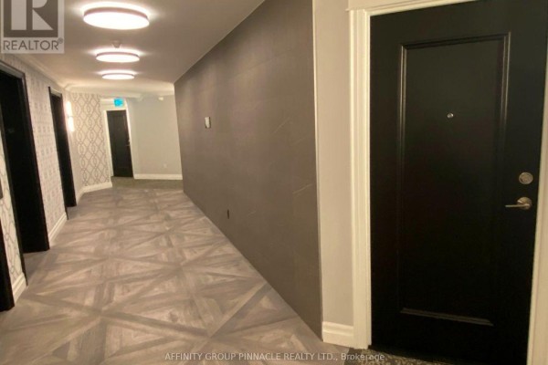 Wide apartment building hallway with patterned wallpaper, dark grey accent wall, and dark doors. - 1301 - 220 Forum Drive, Mississauga