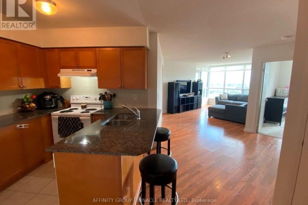 Open concept kitchen and living area with wood cabinets, granite countertops, sofa, and city view. - 1301 - 220 Forum Drive, Mississauga