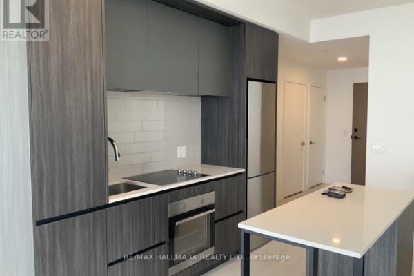 Kitchen area featuring dark wood cabinets, induction cooktop, stainless steel oven, and island. - 1301 - 225 Sumach Street E, Toronto
