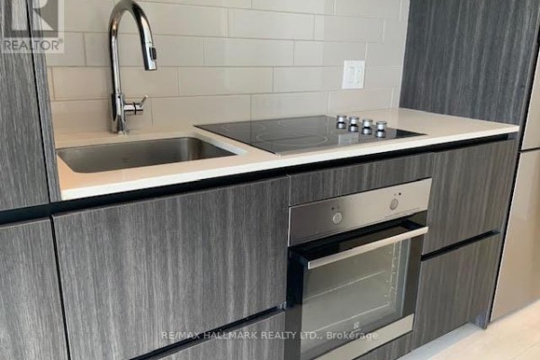 Close-up of a kitchen sink, faucet, induction cooktop, and built-in oven with dark cabinets. - 1301 - 225 Sumach Street E, Toronto