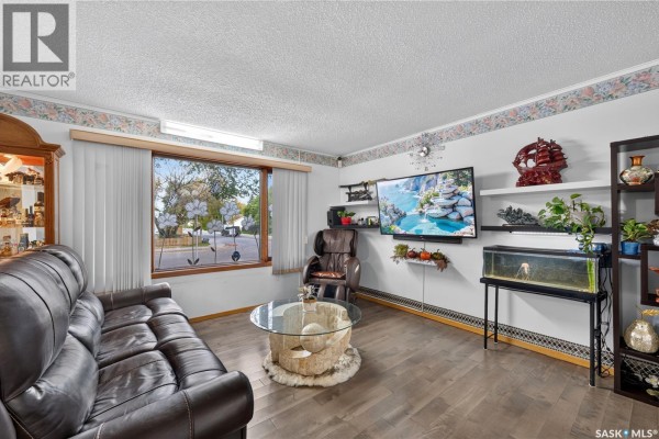 Living room with a large window, dark brown couch, glass coffee table, and mounted TV. - 1301 King Street, Regina