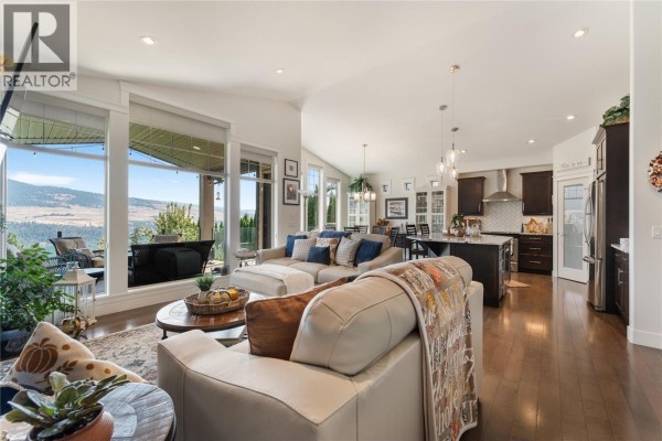 Spacious living room with large windows, a sectional sofa, and an open-concept kitchen. - 13011 East Ridge Drive, Lake Country