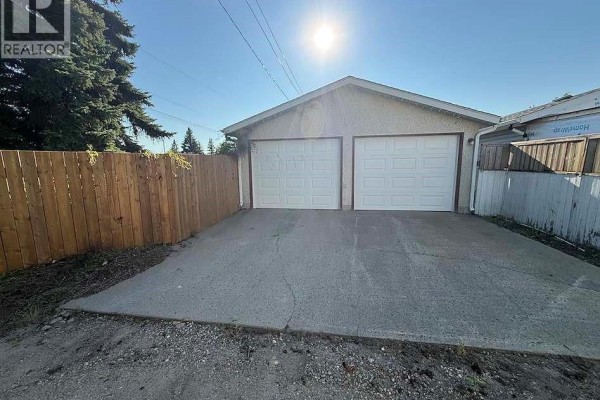 Double garage with two white doors, concrete driveway, and wooden fence on a sunny day. - 1302 112th Street, North Battleford