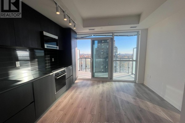 Modern kitchen with black cabinetry, stainless steel appliances, and a view of the city from the balcony. - 1303 - 120 Broadway Avenue, Toronto