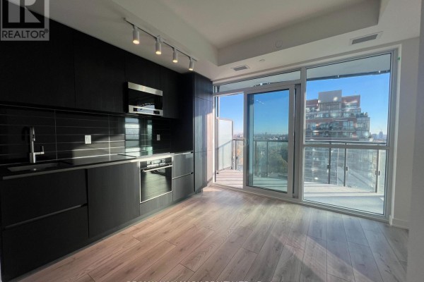 Bright apartment kitchen with dark cabinets and a large sliding glass door leading to a balcony with a city view. - 1303 - 120 Broadway Avenue, Toronto