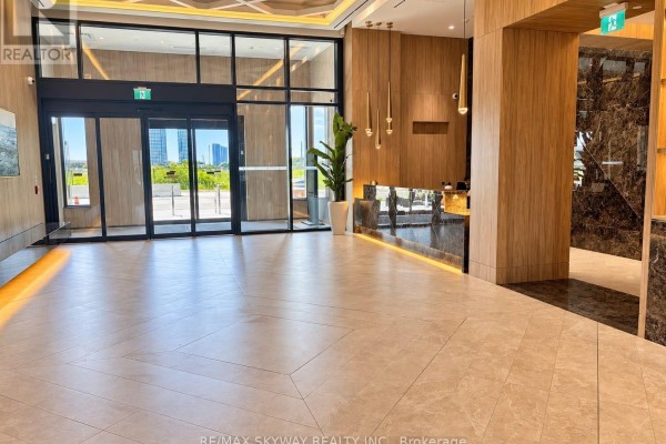 Spacious condominium lobby with glass entrance doors, marble front desk, and wood-paneled walls. - 1303 - 21 Meadowdale Road, Vaughan