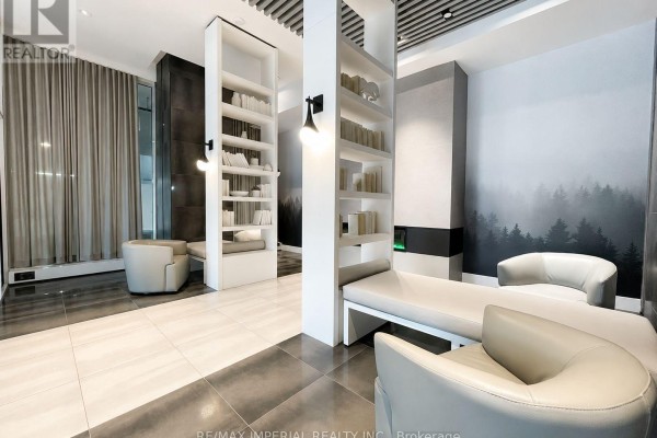 Contemporary lounge area with floor-to-ceiling bookshelves, fireplace, seating, and forest-themed wall art. - 1303 - 2481 Taunton Road, Oakville