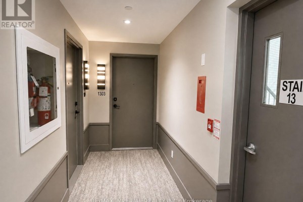 Apartment hallway with grey doors, recessed lighting, fire extinguisher cabinet, and textured carpet. - 1303 - 2481 Taunton Road, Oakville