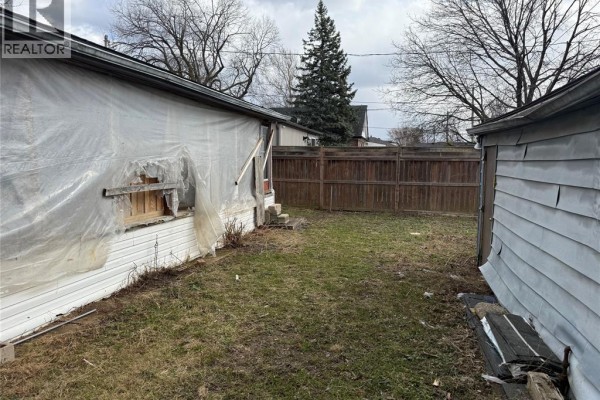View of the side and back of a house with white siding covered by clear plastic sheeting and wooden supports. A brown wooden fence is in the background. - 1303 Central, Windsor