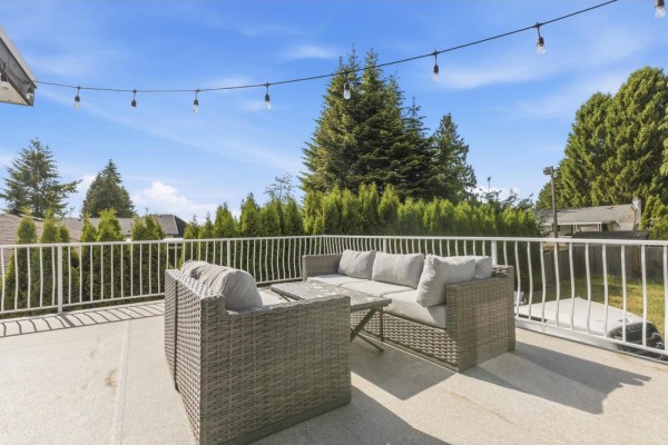 Rooftop patio with wicker furniture and string lights, overlooking trees. - 13035 98a Avenue, Surrey