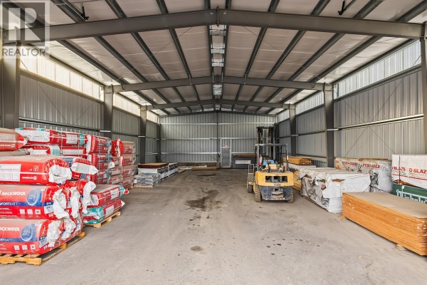Interior of a large steel-framed warehouse with stacked building materials and a forklift. - 1304, 1320, 1334 Industrial Road, West Kelowna
