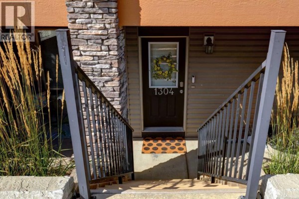Close-up of the front door of townhouse 1304, with stone accents and railings. - 1304, 2461 Baysprings Link Sw, Airdrie