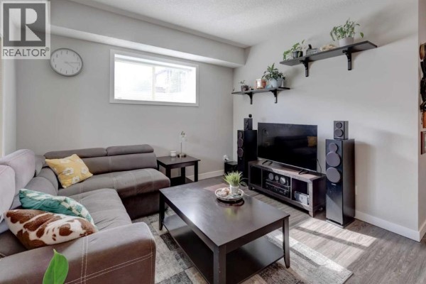 Living room with a sectional sofa, large TV on a media console, and speakers. - 1304, 2461 Baysprings Link Sw, Airdrie