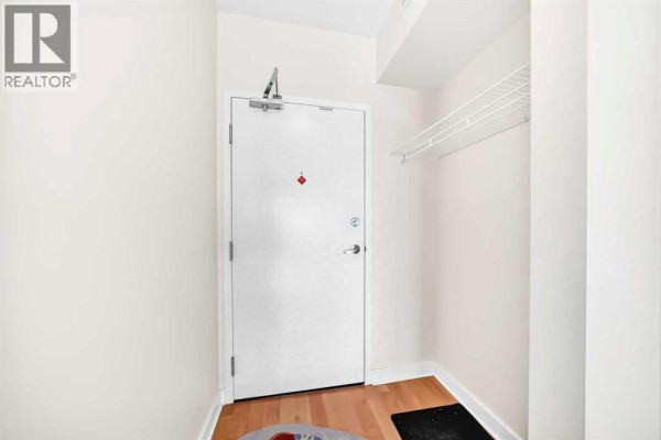 Interior view of an apartment entrance with a white door, wood floor, and a wire shelf. - 1304, 3820 Brentwood  Nw, Calgary