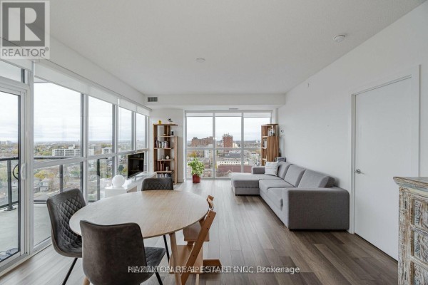 Living room with grey sectional sofa, dining table, and floor-to-ceiling windows overlooking the city. - 1304 - 1604 Eglinton Avenue W, Toronto