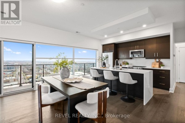 Kitchen island with white stools, dining table with chairs, and large windows with a city view. - 1304 - 1880 Gordon Street, Guelph