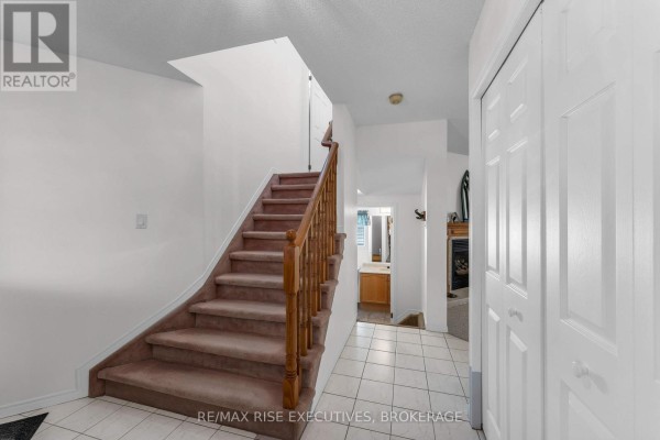 Interior foyer with a carpeted staircase, tiled floor, white doors, and a glimpse of a fireplace. - 1304 Fisher Crescent, Kingston