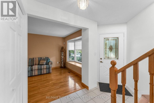 View from the foyer into a living room with hardwood floors, a bay window, and a sofa. - 1304 Fisher Crescent, Kingston