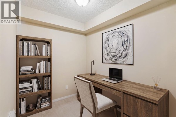 Home office with a wooden desk, bookshelf, laptop, and a chair. - 1305, 8 Bridlecrest Drive Sw, Calgary