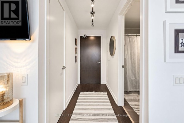 Hallway with dark wood floors, white walls, a dark wood door, and a rug leading to a bathroom. - 1305 - 11 Charlotte Street, Toronto