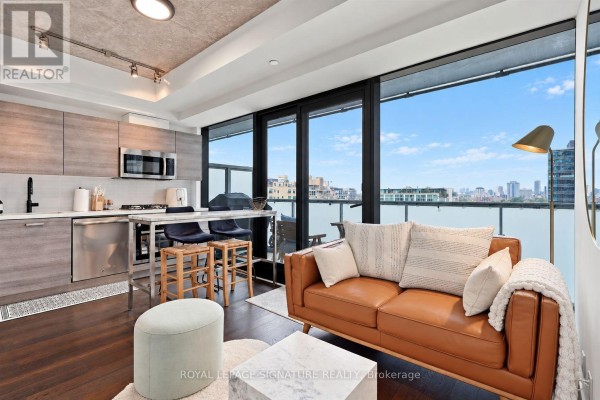 Open concept living room and kitchen with brown sofa, stainless steel appliances, and large windows. - 1305 - 11 Charlotte Street, Toronto
