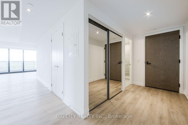 Hallway with white walls, light wood floors, mirrored closet doors, and two white doors. - 1305 - 36 Brentcliffe Road, Toronto