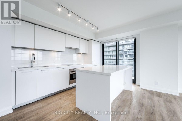 White kitchen with white high-gloss cabinets, stainless steel appliances, a white island, and large windows. - 1305 - 36 Brentcliffe Road, Toronto