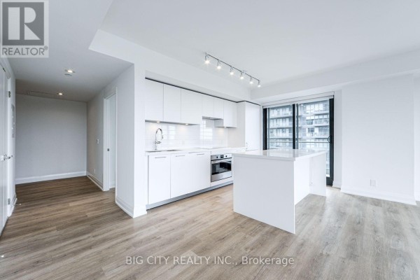 Open concept living area with a white kitchen, light wood floors, and large windows overlooking the city. - 1305 - 36 Brentcliffe Road, Toronto