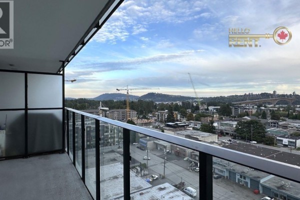 Balcony with glass railing overlooking a city view with water and distant mountains. - 1305 1401 Hunter Street, North Vancouver