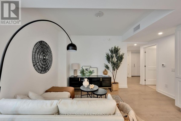 Living room with a large sectional sofa, black media console, and a tall arc floor lamp. - 1306 - 340 Queen Street, Ottawa