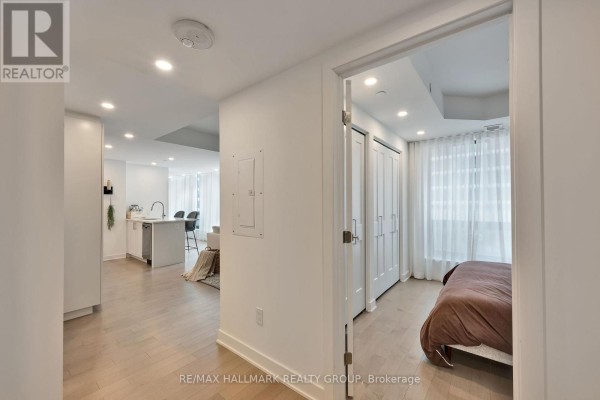 Hallway looking towards an open-concept kitchen and a bedroom with white sheer curtains. - 1306 - 340 Queen Street, Ottawa