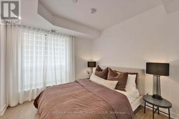 Bedroom with a king-size bed, side tables, and large white sheer curtains covering the window. - 1306 - 340 Queen Street, Ottawa