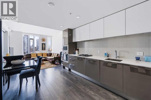 Open concept kitchen and living area with dark wood floors and white countertops. - 1307, 901 10 Avenue Sw, Calgary