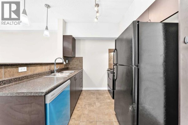 Kitchen counter space with stainless steel sink, dark brown cabinets, and a blue dishwasher. - 1308, 604 East Lake Boulevard Ne, Airdrie