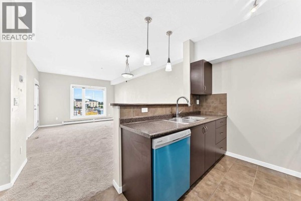 View of the kitchen and living room with a balcony door and a large window. - 1308, 604 East Lake Boulevard Ne, Airdrie