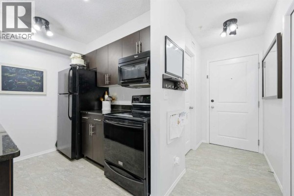 Galley kitchen with dark wood cabinets, black appliances, granite countertops, and light grey flooring. - 1308, 625 Glenbow Drive, Cochrane