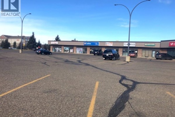Parking lot view of the commercial strip mall with cars parked in front of various businesses. - 1308 2a Street W, Brooks