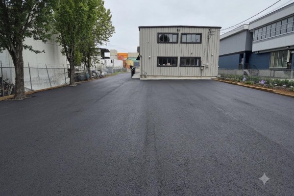 Asphalt driveway leading to a commercial building with grey metal siding and many windows. - 13087 116 Avenue, Surrey