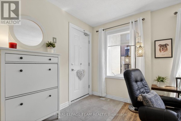 Entryway of the townhouse featuring a white door, shoe cabinet, round mirror, and chair. - 130a Lindenshade Drive, Ottawa