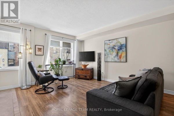 Living room with light beige walls, wood-look flooring, sofa, chairs, and a television. - 130a Lindenshade Drive, Ottawa