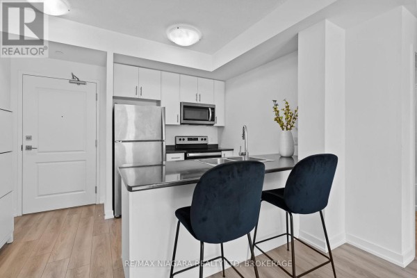 Kitchen with white cabinets, stainless steel appliances, and a breakfast bar with two blue chairs. - 131 - 5055 Greenlane Road, Lincoln
