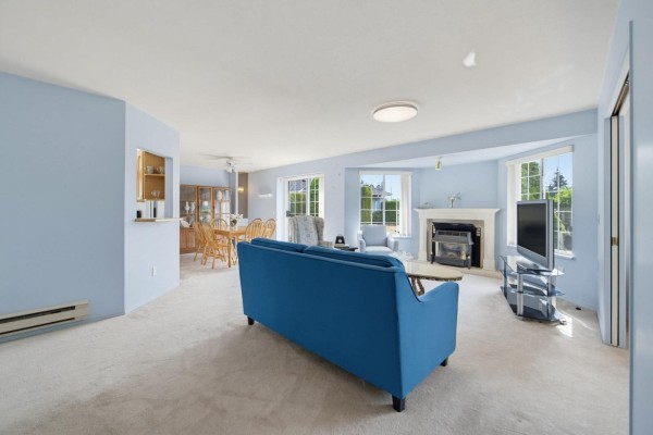 Living room with blue sofa, two armchairs, carpet, dining area, and large windows. - 131 1450 Mccallum Road, Abbotsford