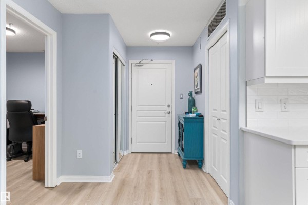 Apartment hallway with light blue walls, wood-look flooring, white doors, and a decorative teal cabinet. - #131 16035 132 St Nw, Edmonton
